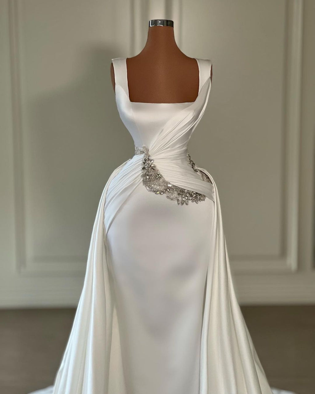 Vestido de novia largo color marfil con tirantes en forma de A, sin mangas, con joyas y cola.