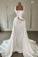 Vestido de novia largo color marfil con tirantes en forma de A, sin mangas, con joyas y cola.